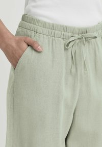 Jogging en lin mélangé vert clair avec une taille élastique et un cordon de serrage, comportant des poches latérales et un tissu texturé.