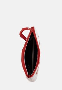 Pochette rossa e bianca con zip, dal rivestimento texturizzato e manico ad anello; l'interno mostra una fodera nera con oggetti trasparenti visibili all'interno.