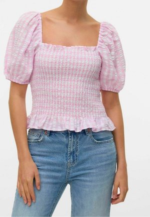 Femme portant un haut froncé à rayures roses et blanches avec manches bouffantes et ourlet à volants, associé à un jean en denim bleu.