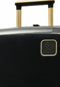 Maleta rígida negra con una superficie elegante, mango telescópico dorado y un logo cuadrado con "Mandarina Duck" grabado.