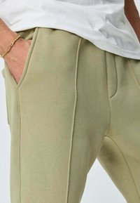 Un pantalon de survêtement vert clair en tissu doux, avec une coupe ajustée, des coutures précises, des poches latérales et une taille confortable.