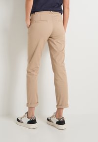 Pantalons beiges avec des ourlets retroussés et des poches arrière, associés à des baskets au motif léopard et aux accents noirs.