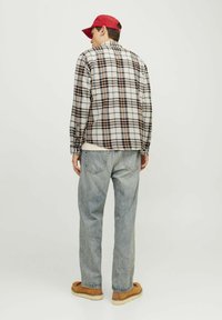 Gegチェックshirt in beige, bruin en zwart, gecombineerd met lichtblauwe losse jeans en bruine schoenen. Geassorteerd met een rode pet.