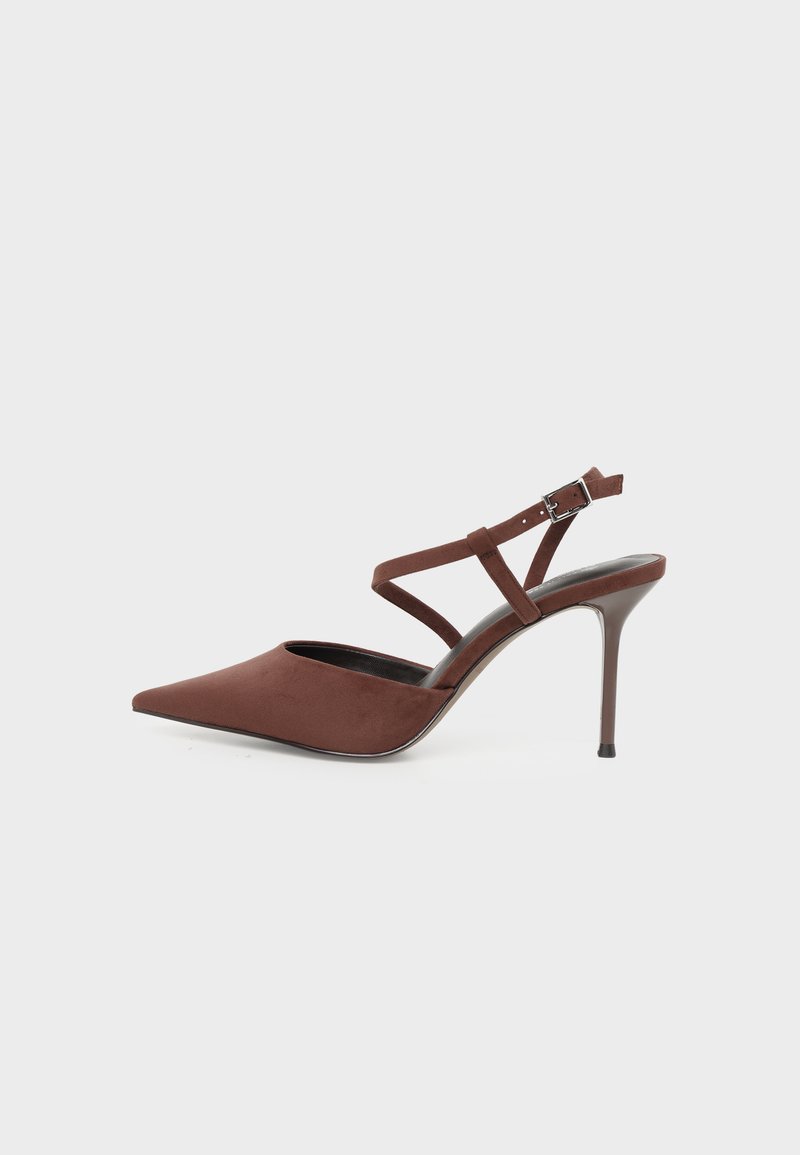 Chaussure à talon haut marron à bout pointu avec des lanières fines à la cheville et une petite boucle sur un fond clair.