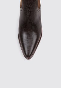 Chaussure en cuir marron à bout pointu avec une finitiontexturée et des découpes sur les côtés, présentant une semelle lisse et une silhouette épurée.