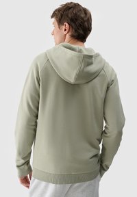 Felpa verde in cotone misto con cappuccio, polsini e orlo a costine. La parte posteriore presenta una texture liscia e dettagli delle cuciture.