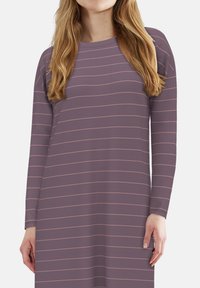 Woman wearing a long-sleeve, purple dress with thin, horizontal pink stripes and loose blonde hair against a plain background.