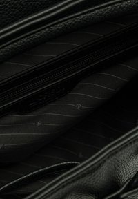 Interior de un bolso de mano de cuero negro con un compartimento con cremallera. El forro presenta un patrón a rayas en tonos de negro y gris.