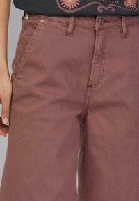Bordeaux wijde broek van denim. Kenmerken zijn onder andere een knoopsluiting, voorzakken en zichtbare stikseldetails. Glad textuur.