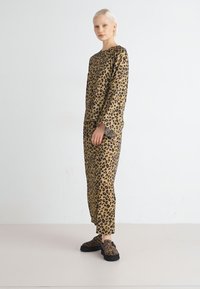 Sada domácího oblečení s leopardím vzorem v béžových tónech, zahrnující volné tričko a kalhoty s dlouhými rukávy a kotníkovým střihem, doplněná o odpovídající boty.