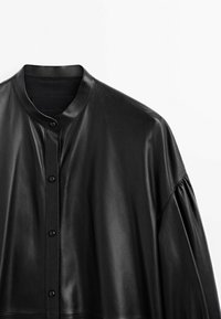 Chemise noire en cuir avec des boutons, col rond et manches longues légèrement froncées, sur fond blanc uni.