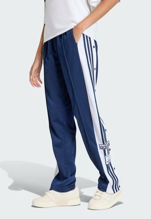 Granatowe spodnie dresowe z białymi paskami i napami po bokach. Wykonane z gładkiego materiału, posiadają kieszenie oraz detal z logo marki.