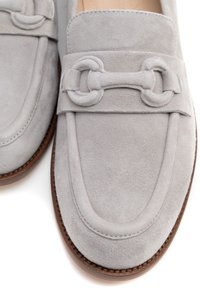 Mocassini in suede grigi con finitura liscia, dotati di una fascia decorativa e dettagli metallici, e una suola marrone a contrasto.