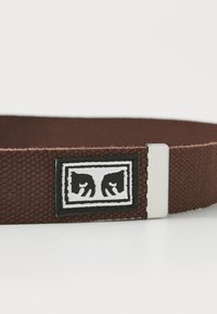 Brown woven fabric belt with silver metal buckle and a black and white patch featuring two stylized horse heads facing each other.