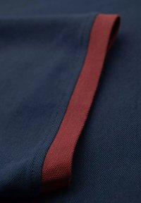 Tela azul marino con una textura suave que presenta un borde en burdeos contrastante, mostrando un ligero brillo y un sutil detalle de costura.