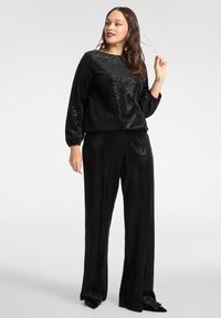 Czarna bluzka z cekinami z długim rękawem i okrągłym dekoltem, zestawiona z czarnymi spodniami o szerokich nogawkach również pokrytymi cekinami. Gładka faktura z refleksyjną powierzchnią.