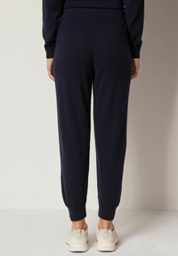 Marinblå joggingbyxor med avsmalnande passform, ribbade muddar och elastisk midja; matchas med lätta skor, på en neutral bakgrund.