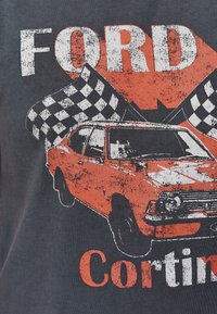 Grå T-shirt med et slidt grafisk motiv af en rød Ford Cortina bil, med sort-hvide ternede flag og "FORD" tekst.