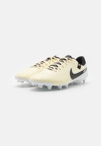 Sárga és fehér focicipők texturált felsőrésszel, fekete Nike Swoosh logóval és fehér, formázott stoplival a tapadásért.