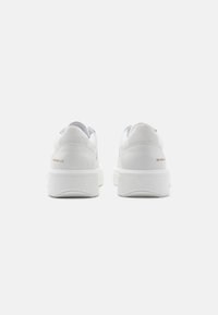 Zapatillas de plataforma de cuero blanco con textura suave, tacón redondeado y diseño minimalista; incluye un sutil logotipo en dorado en el tacón.