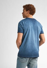 Camiseta de algodón azul degradado de manga corta, fabricada en una tela suave, con un cuello redondo y acentos en azul oscuro contrastantes en las mangas.
