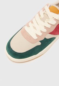 Sneaker multicolore con tessuto perforato beige, dettagli in suede verde, sovrapposizioni rosa e rosse e lacci crema. Suola in gomma testurizzata.