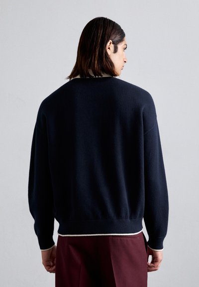 Pulover tricotat bleumarin cu o croială lejeră, manșete rib și un guler interior deschis la culoare care contrastează. Design simplu, textură moale.