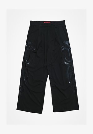 Črne široke hlače z naborki spredaj, z sijočimi črnimi tribal vzorci na straneh in rdečim pasom z blagovno znamko.