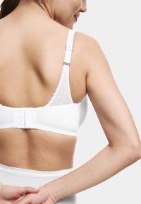 Sujetador blanco con material suave, detalles de encaje en la parte posterior, tirantes ajustables y cierre de gancho y ojo.