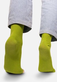 Zielone skarpetki do kostek z miękkiej bawełny, z prążkowaną fakturą i otwartym palcem, noszone z jasnoniebieskimi dżinsami.