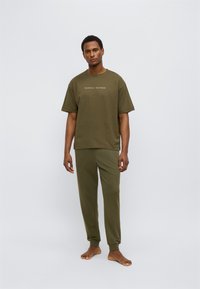 Σετ άνετων ρούχων από βαμβάκι σε ελιά πράσινο, περιλαμβάνει κοντομάνικο T-shirt και παντελόνια με στενή εφαρμογή. Το T-shirt φέρει το λογότυπο "TOMMY HILFIGER" στην μπροστινή πλευρά.