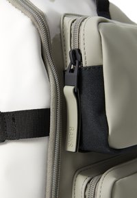 Grau gefärbter Rucksack aus glattem, wasserdichtem Material, mit kontrastierendem dunklem Stofffach und einem robusten Reißverschluss mit einem markierten Ziehband.