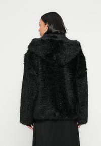 Czarna kurtka z futerka ekologicznego z kapturem, posiadająca fakturowaną powierzchnię, długie rękawy oraz pudełkowy krój, zaprojektowana z myślą o ciepłe i wygodzie.