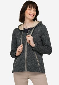 Mörkgrå zip-up jacka med en ljusbeige huva. Har dragkedjefickor och dragsnören med logotypdetaljer. Mjuk, texturerad tyg.