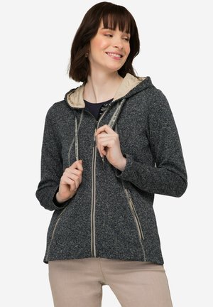 Veste zippée gris foncé avec une capuche beige clair. Comprend des poches zippées et des cordons de serrage avec des accents de logo. Tissu doux et texturé.