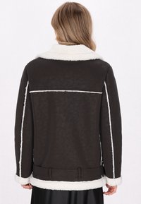 Braune Kunstfelljacke mit weißem Kragen und Manschetten, ausgestattet mit einem taillierten Design, gerader Passform und einer strukturierten Oberfläche.