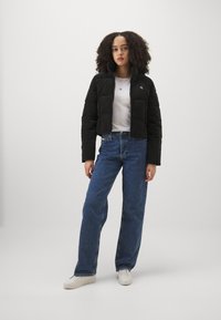 Sort cropped pufferjakke med høj krave, parret med en hvid T-shirt, blå højtaljede jeans og hvide sneakers.