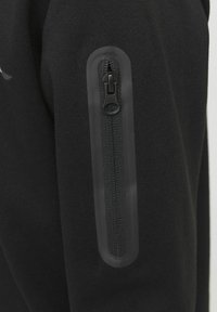 Svart sweatshirt med en zippered ficka på överarmen, tillverkad av mjukt tyg med en slät textur och minimalistisk design.