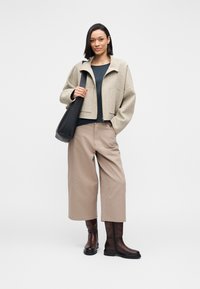 Beżowa krótka kurtka z mieszanki wełny, ciemnoniebieski top, beżowe spodnie o szerokich nogawkach oraz brązowe kozaki za kolano, zestawione z czarną torebką.