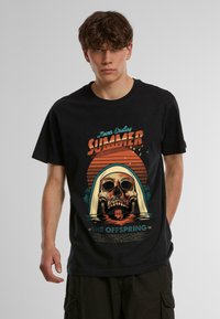 Sort bomulds-T-shirt med en grafisk design af et kranium med hætte, farverig tekst og solnedgangsbilleder. Korte ærmer og rund hals.