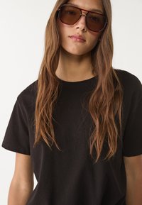 Czarna bawełniana koszulka z luźnym krojem i krótkimi rękawami, w połączeniu z dużymi brązowymi okularami przeciwsłonecznymi o geometrycznym wzorze ramki.