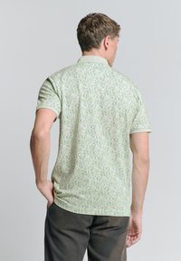 Lichtgroen polo shirt met een herhalend bladdessign, korte mouwen en een kraag, gemaakt van een gladde stof.