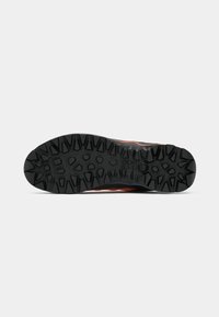 Hardloopschoen zool van robuust zwart rubber, met een diep, hoekig profiel voor grip. Versterkte randen en gestructureerd oppervlak.