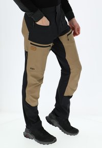 Taktiska utomhusbyxor med en blandning av khaki- och svarta tyger, fickor med dragkedja och en åtsittande design. Hållbart och funktionellt material.
