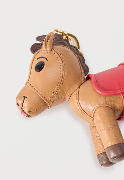 Μπρελόκ σε σχήμα αλόγου από καφέ δέρμα με μαύρα μάτια κουμπιά, ραμμένες λεπτομέρειες και κόκκινο σέλα σε λευκό φόντο.