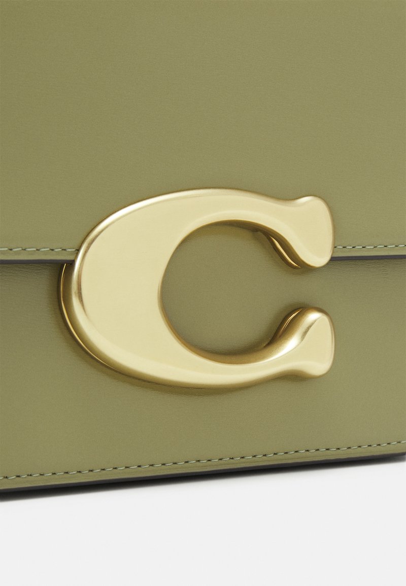 Olivgrüne Lederhandtasche mit einem auffälligen goldfarbenen Metallverschluss in Form eines "C", der eine glatte Textur und kontrastierende Nähte aufweist.