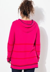 Różowy sweter z kapturem w czerwone i granatowe poziome paski, długie rękawy i luźny krój. Wykonany z miękkiego materiału o fakturowanym wykończeniu.