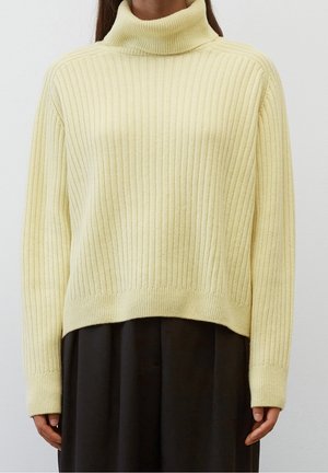 Geel geribd turtleneck sweater met lange mouwen; zachte textuur, losse pasvorm en een iets verkorte zoom. Draagt over een zwart kledingstuk.