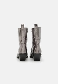 Ghete de gleznă metalice argintii cu vârfuri ascuțite, suprafață texturată și tocuri scurte. Include închidere cu fermoar și tab-uri de prindere în partea din spate.