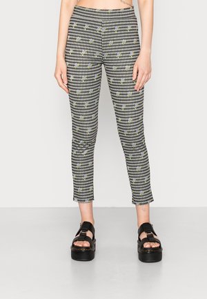 Leggingstijl broeken met zwart-wit geruit patroon en kleine paarse bloemen, gedragen met zwarte platformsandalen.